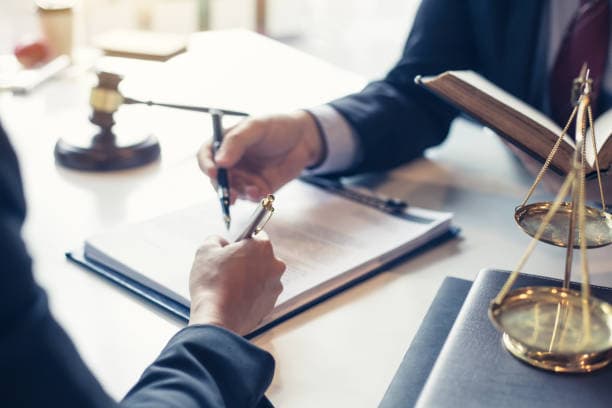 Avocat signant un document a cote d'un marteau de juge et d'une balance